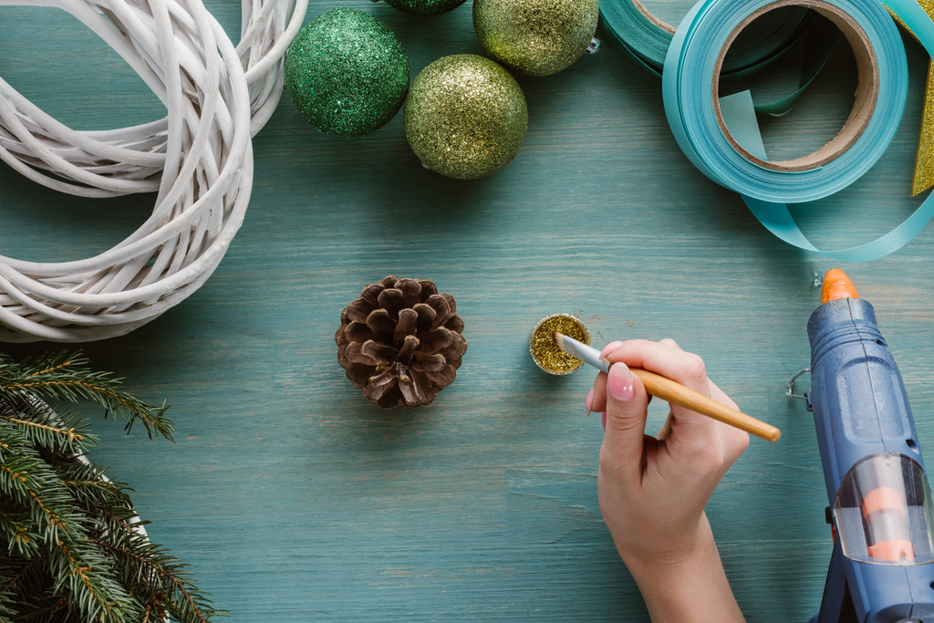 partial view of woman coloring pine cone with golden paint on blue wooden surface - Photo, Image