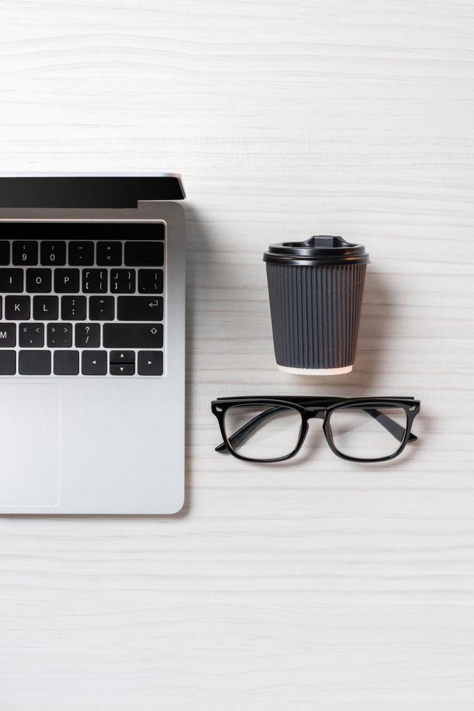 верхний вид устроенный ноутбук, очки и бумажная чашка кофе за столом в офисе, минималистическая концепция
  - Фото, изображение