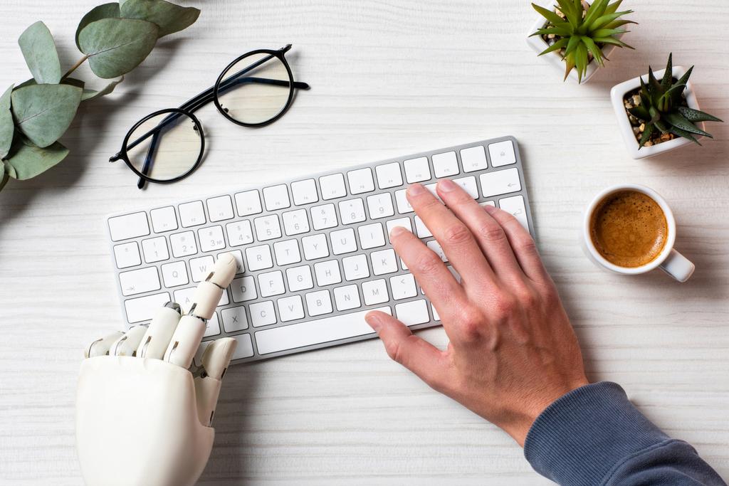 обрезанный образ бизнеса с протезной рукой, печатающей на клавиатуре компьютера за столом в офисе
  - Фото, изображение