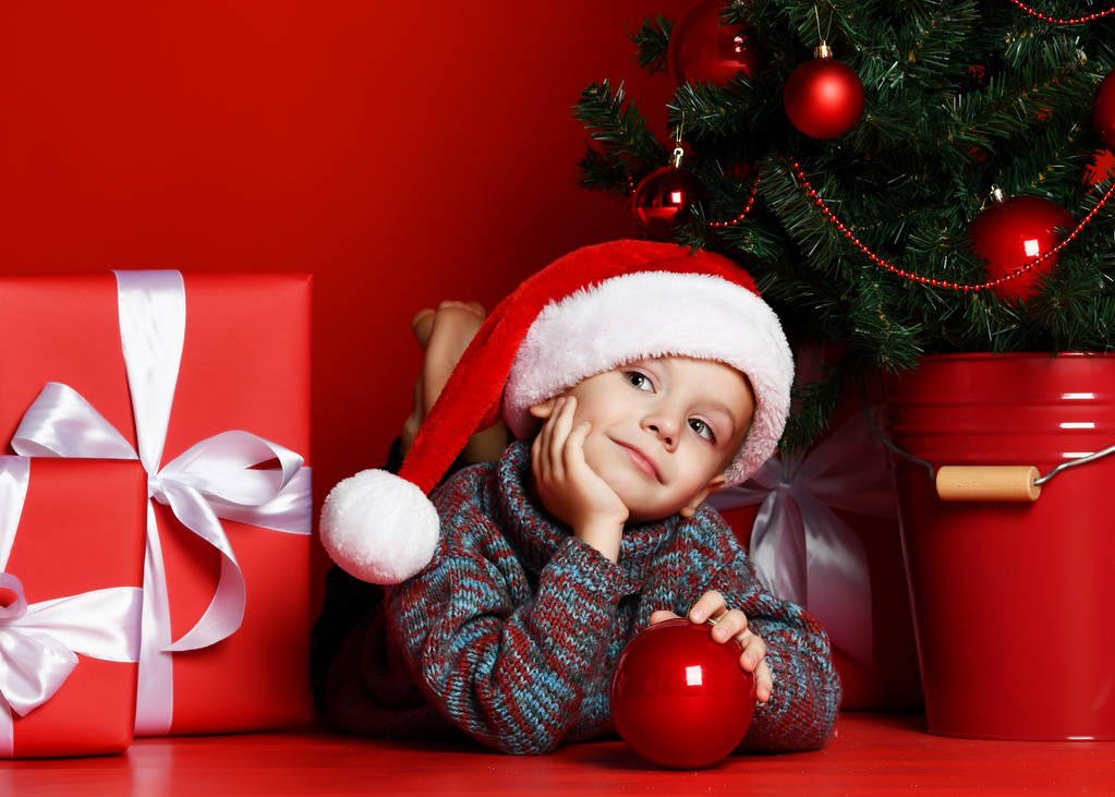 Zabawne dziecko uśmiechający się w Santa czerwony kapelusz leżącego na na tle choinki - Zdjęcie, obraz