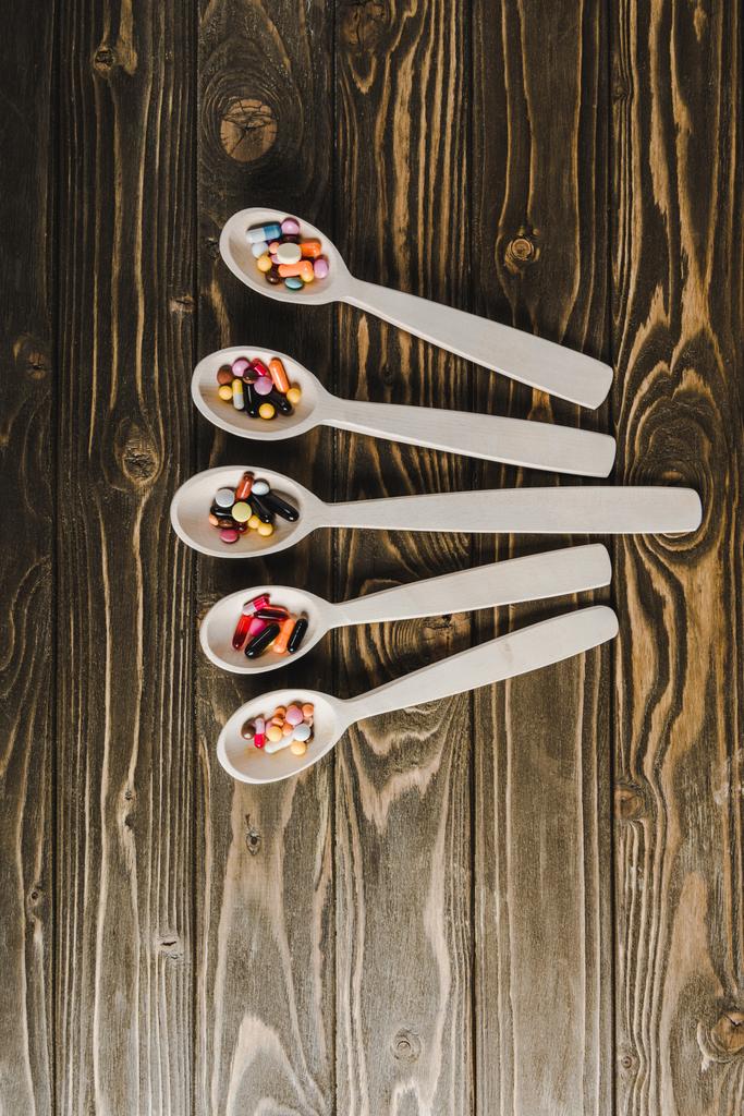 bovenaanzicht van vijf lepels met pillen op houten tafelblad - Foto, afbeelding