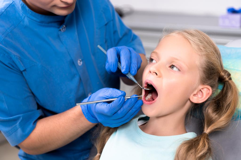 обрезанный снимок стоматолога с инструментами изучения зубов маленького ребенка
 - Фото, изображение