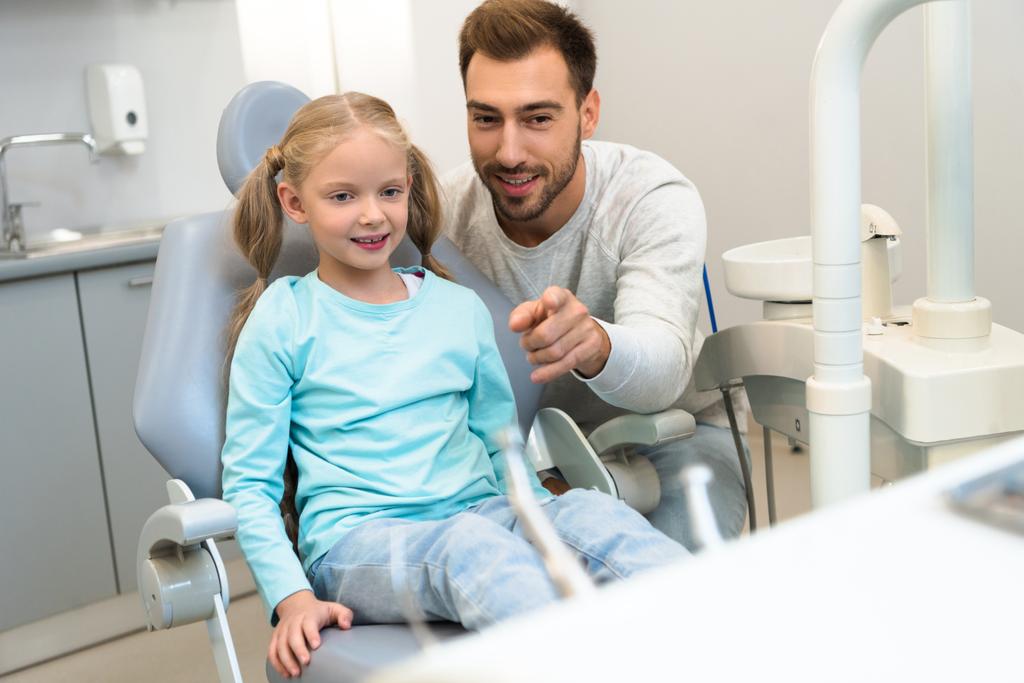father and daughter in dentist office looking at stand with tools  - Photo, Image