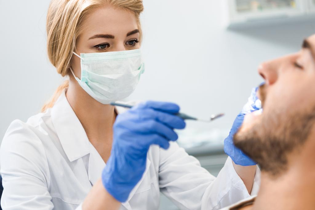 Młoda kobieta dentysty badanie zębów przystojny uśmiechający się klienta - Zdjęcie, obraz