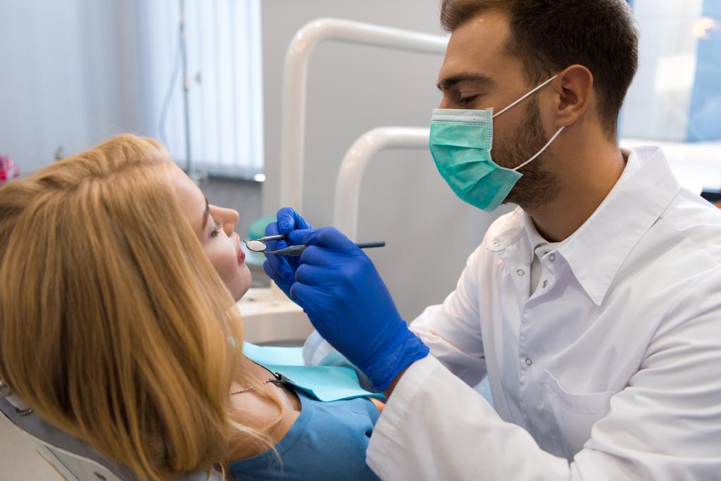 schöner junger Zahnarzt untersucht Zähne weiblicher Klientin - Foto, Bild