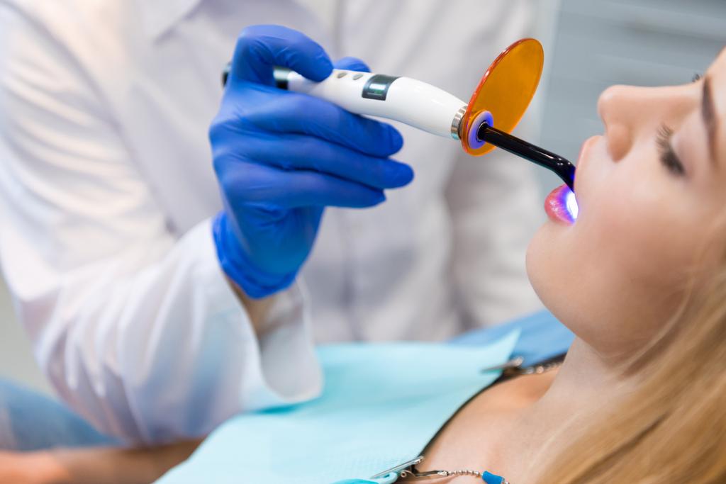 女性のクライアントの使用する歯科硬化光と手袋で歯科医のショットをトリミング - 写真・画像