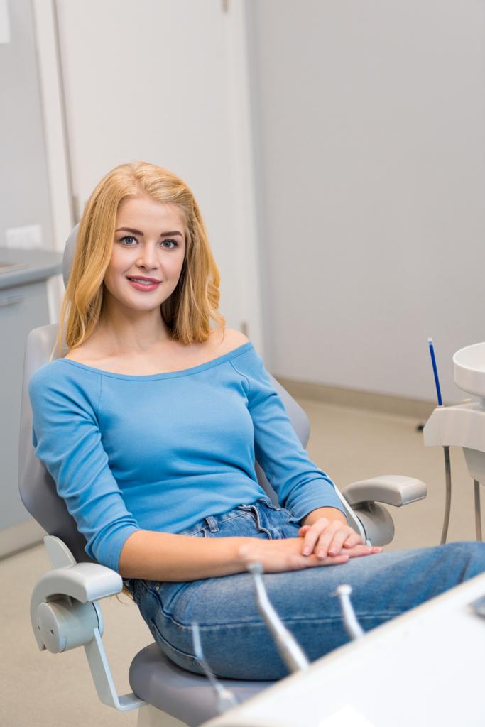 Szczęśliwa młoda kobieta siedzi w Fotel dentystyczny w gabinecie stomatologicznym i patrząc na kamery - Zdjęcie, obraz