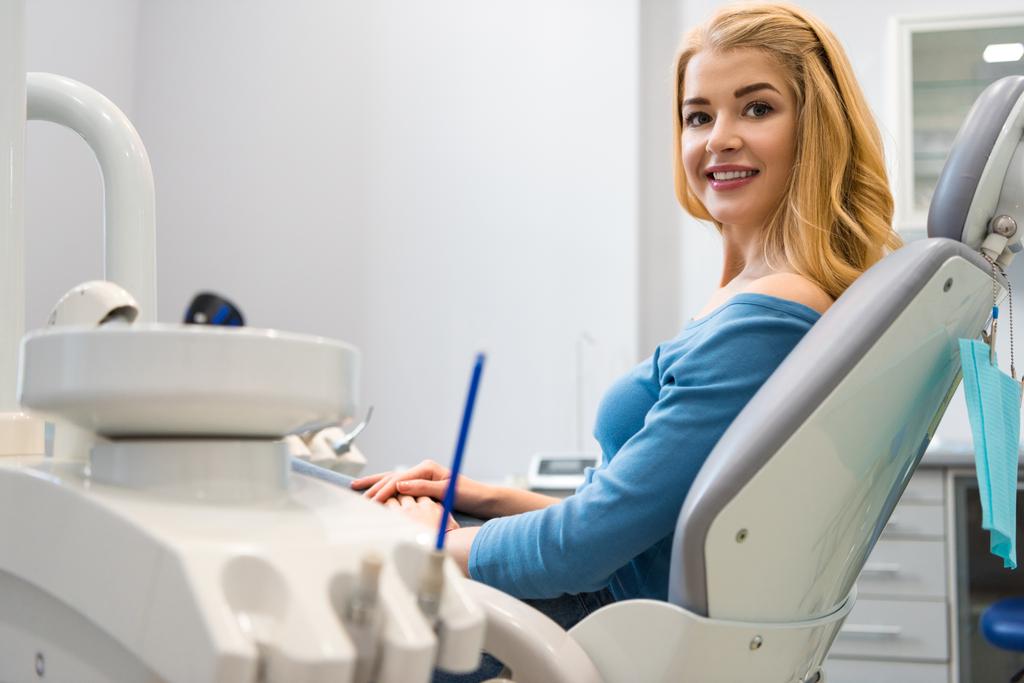 усміхнена молода жінка сидить у стоматологічному кріслі в кабінеті стоматолога
 - Фото, зображення