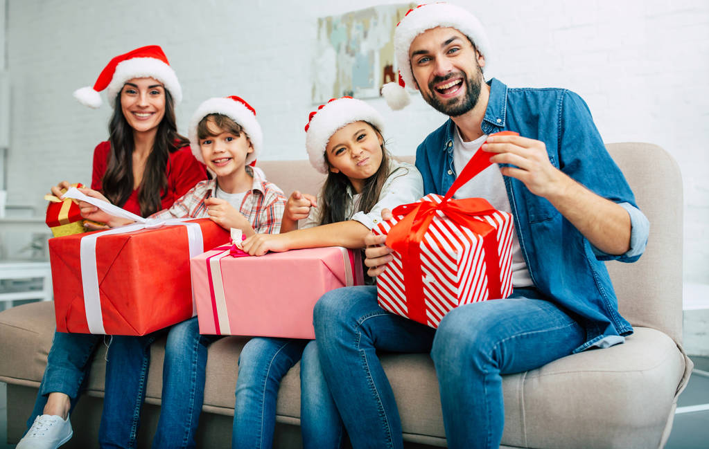 クリスマス プレゼント サンタ帽子で若い家族は、リビング ルーム - 写真・画像
