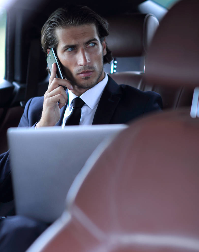 Бизнесмен в машине с ноутбуком разговаривает по телефону
 - Фото, изображение