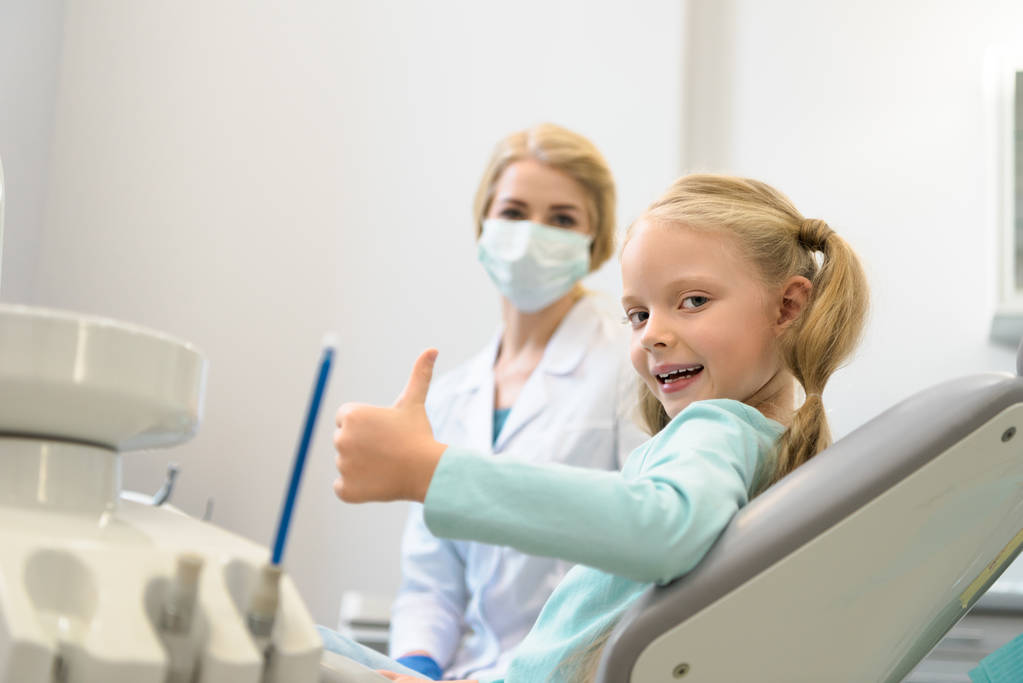 beautiful little child showing thumb up while sitting in chair at dentist office - Photo, Image