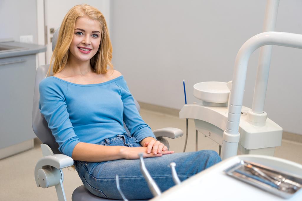 Ευτυχισμένη νεαρή γυναίκα που κάθεται στην οδοντιατρική καρέκλα στο οδοντιατρείο - Φωτογραφία, εικόνα