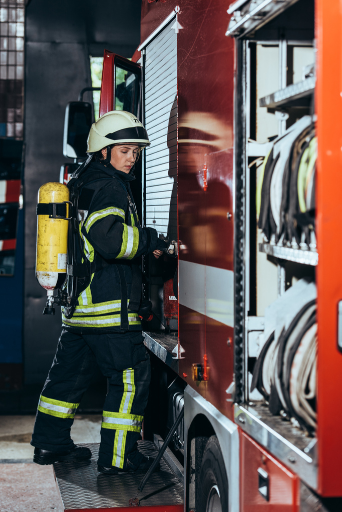 boční pohled na ženské hasič s hasicí přístroj na zpět uzavírací vůz na hasičské stanici - Fotografie, Obrázek