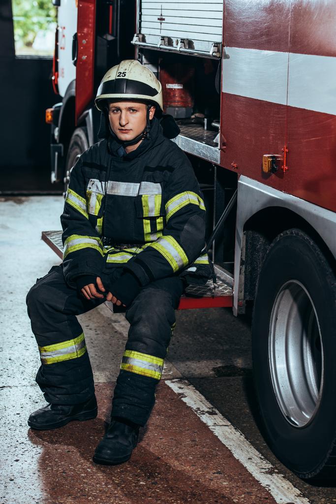 bombero masculino en uniforme y casco en camión de bomberos en el departamento de bomberos
 - Foto, Imagen