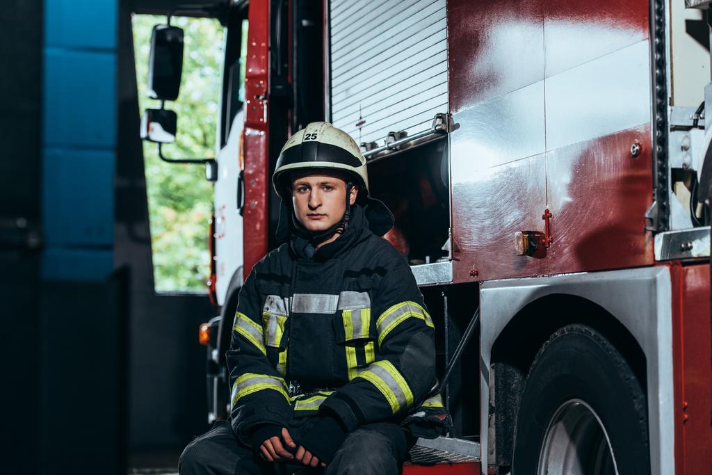 Portret van mannelijke brandweerman in uniform en helm op vrachtwagen brand brandweer - Foto, afbeelding