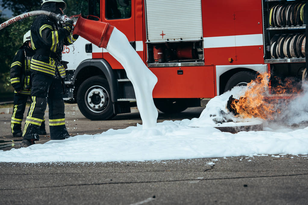 частичный вид пожарного, тушащего огонь пеной на улице
 - Фото, изображение