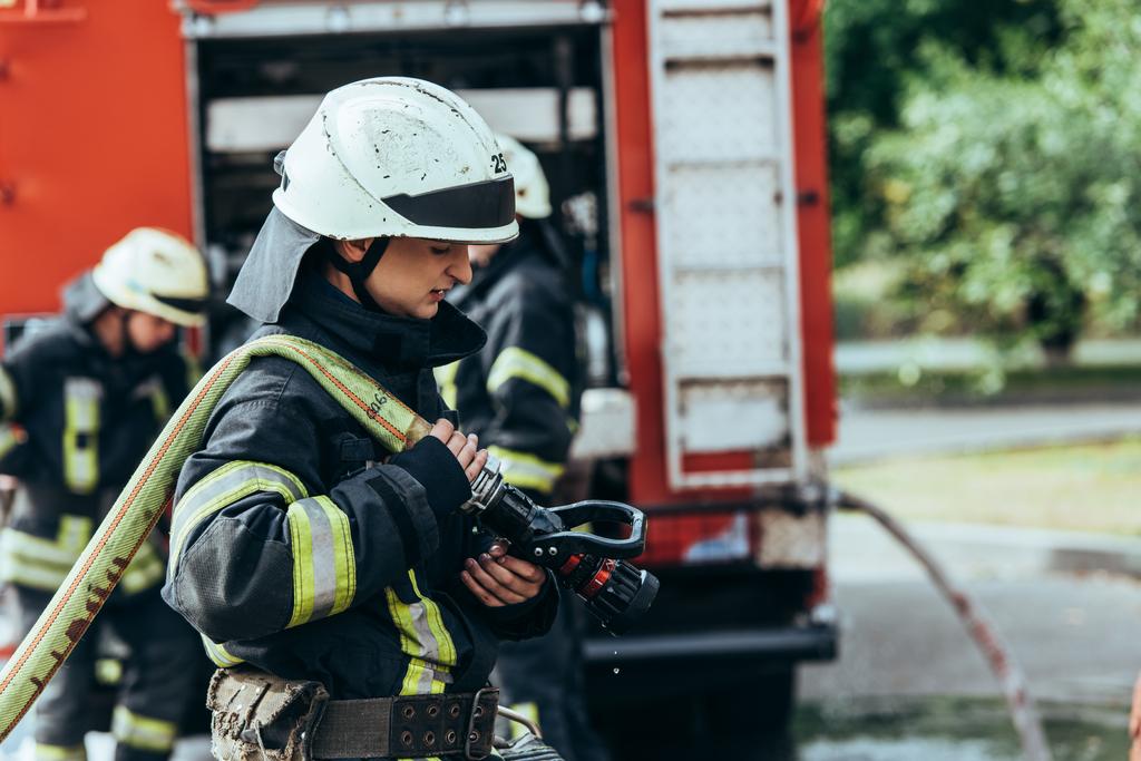 вибірковий фокус чоловічого пожежного в шоломі з водяним шлангом на вулиці
 - Фото, зображення