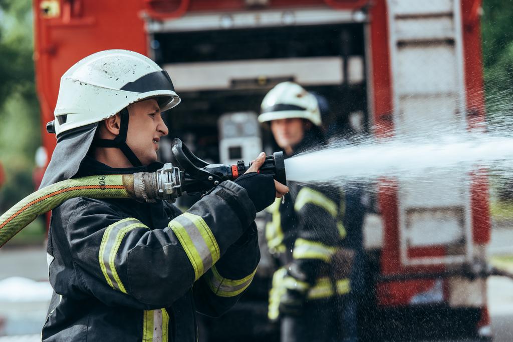 επιλεκτική εστίαση του πυροσβέστη με μάνικα νερό κατάσβεσης πυρκαγιάς στην οδό - Φωτογραφία, εικόνα