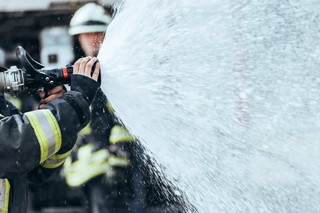 częściowy widok strażaka z wąż wody gaszenia pożaru na ulicy - Zdjęcie, obraz