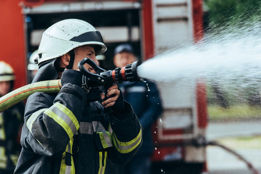 foco selectivo del bombero con manguera de agua extinguiendo el fuego en la calle
 - Foto, Imagen