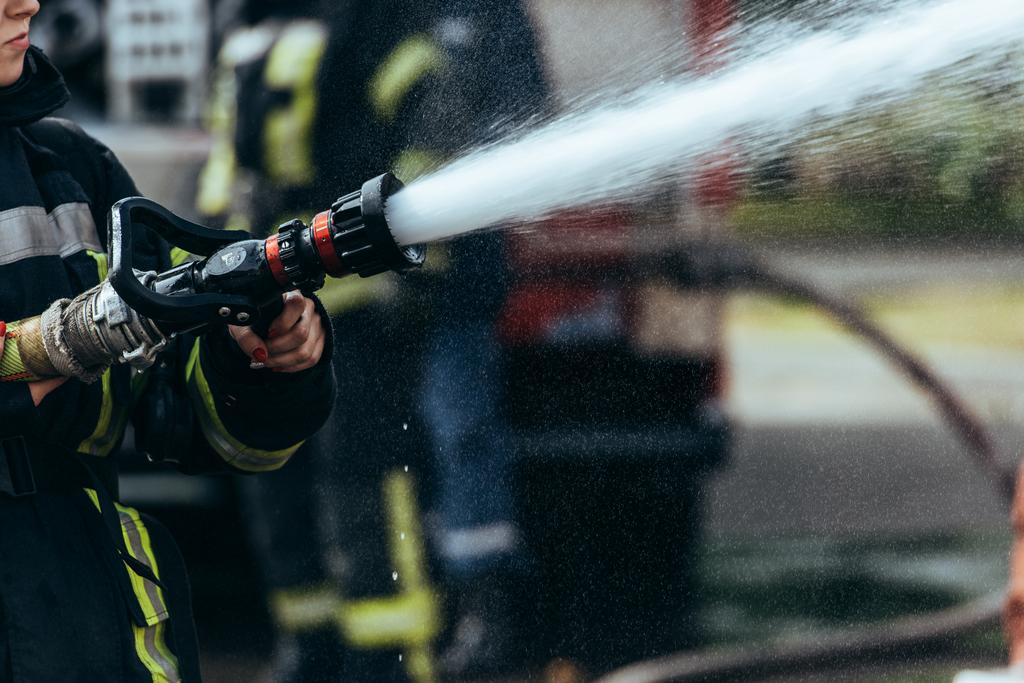 visão parcial do bombeiro com mangueira de água extinguindo incêndio na rua
 - Foto, Imagem