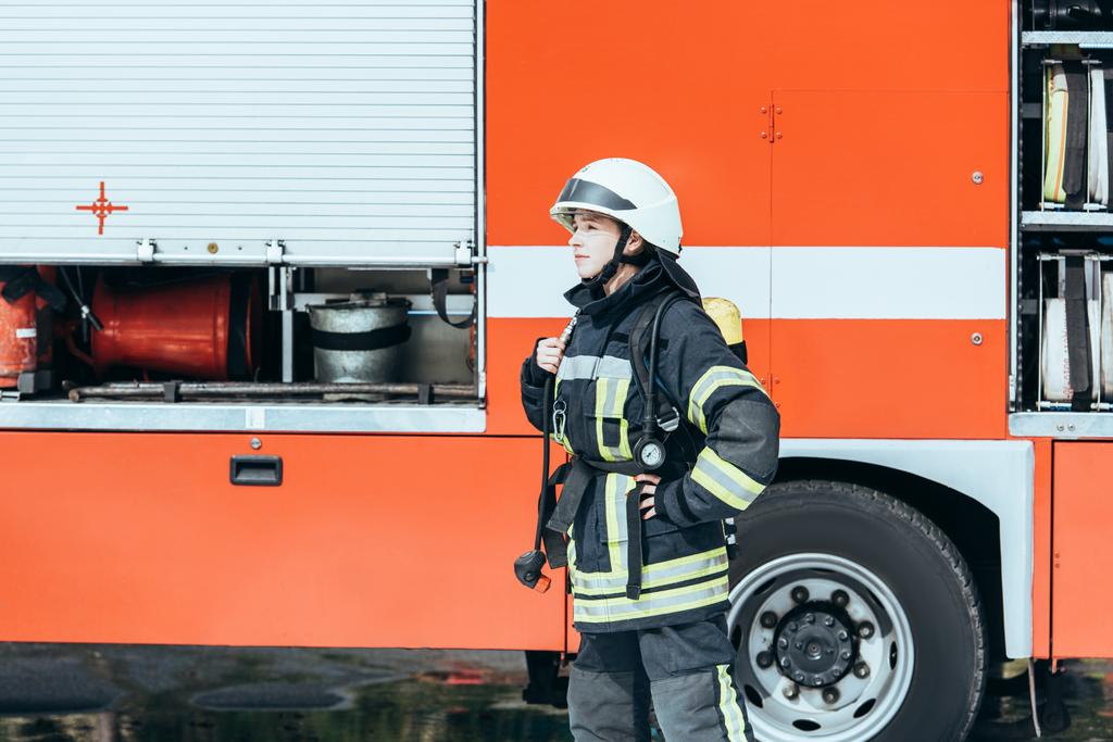 bombero femenino en uniforme protector parado en la calle con camión de bomberos rojo detrás
 - Foto, Imagen
