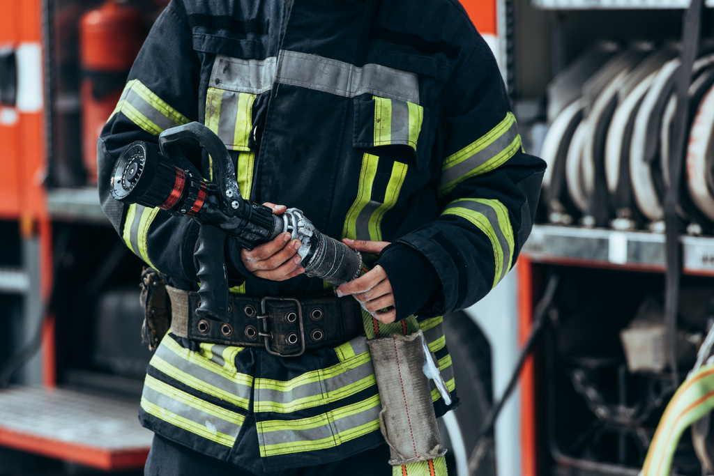 Schnappschuss von Feuerwehrmann in Schutzuniform, der Wasserschlauch in der Hand hält - Foto, Bild