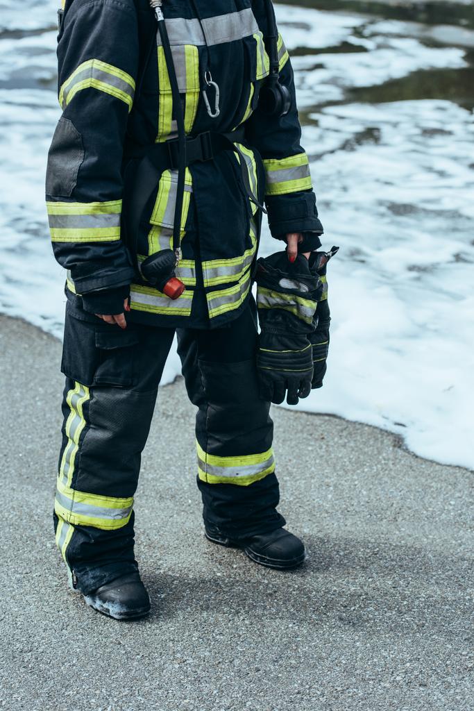 Μερική άποψη της γυναικείας πυροσβέστης σε πυρίμαχο στολή με γάντια χέρι στέκεται steet με αφρό - Φωτογραφία, εικόνα
