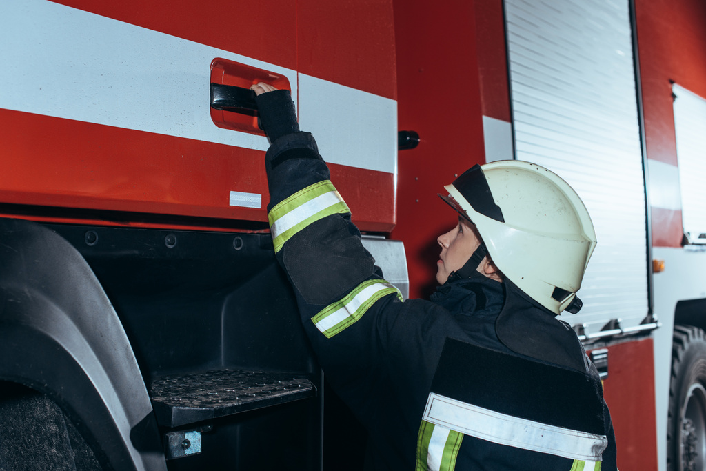 boční pohled na ženské hasič držící kliku truck hasiči - Fotografie, Obrázek