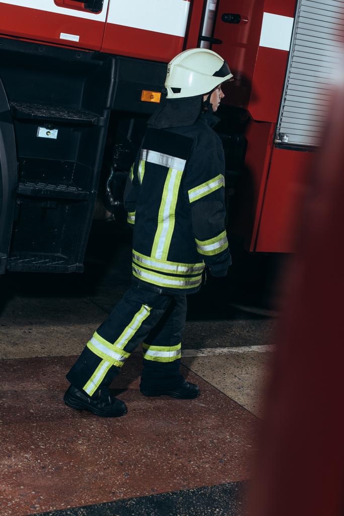 vrouwelijke brandweerman in uniform en helm wandelen op brand station - Foto, afbeelding