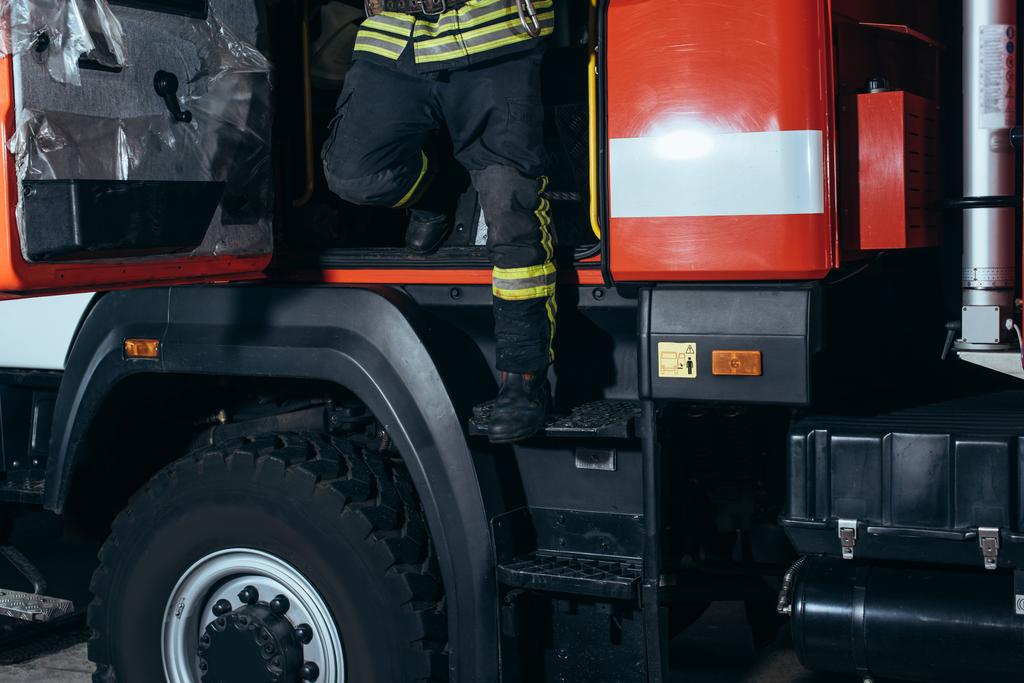 частичный обзор пожарного в огнеупорной форме, выходящего из грузовика на пожарной станции
 - Фото, изображение