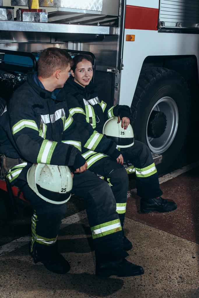 Feuerwehrleute in Schutzuniform unterhalten sich in der Nähe eines Lastwagens an der Feuerwache - Foto, Bild