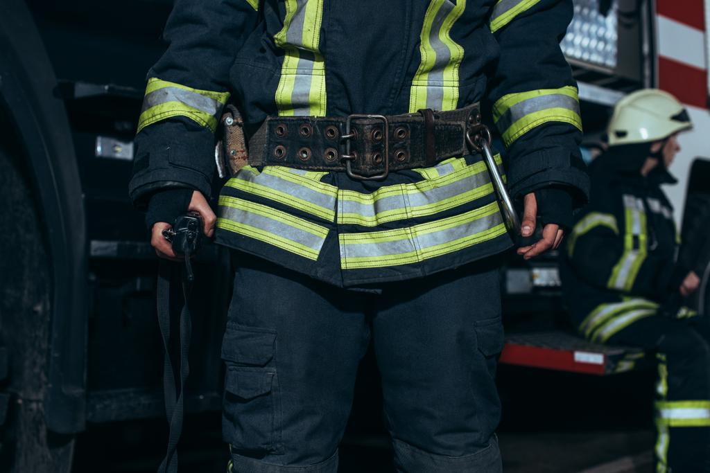 Schuss auf Feuerwehrmann in feuerfester Uniform und Kollegen im Feuerwehrhaus - Foto, Bild