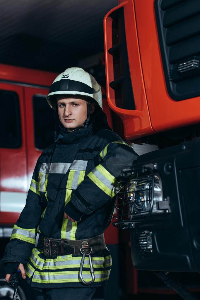 portrait of firefighter in uniform and helmet leaning on truck at fire station - Photo, Image