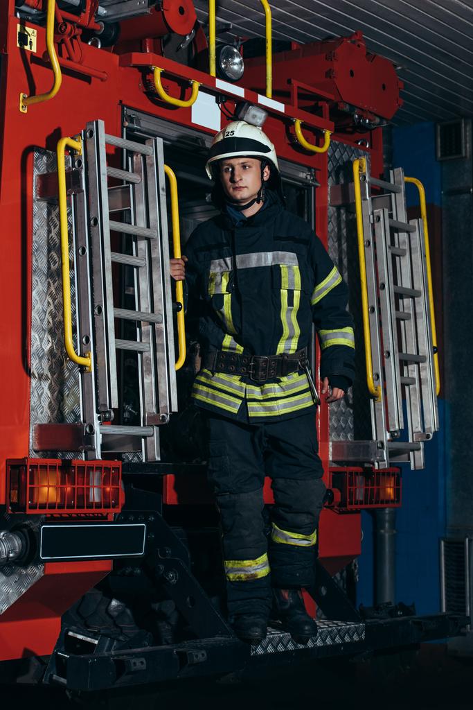 пожежник в захисній формі і шолом, що стоїть на вантажівці на пожежній станції
 - Фото, зображення