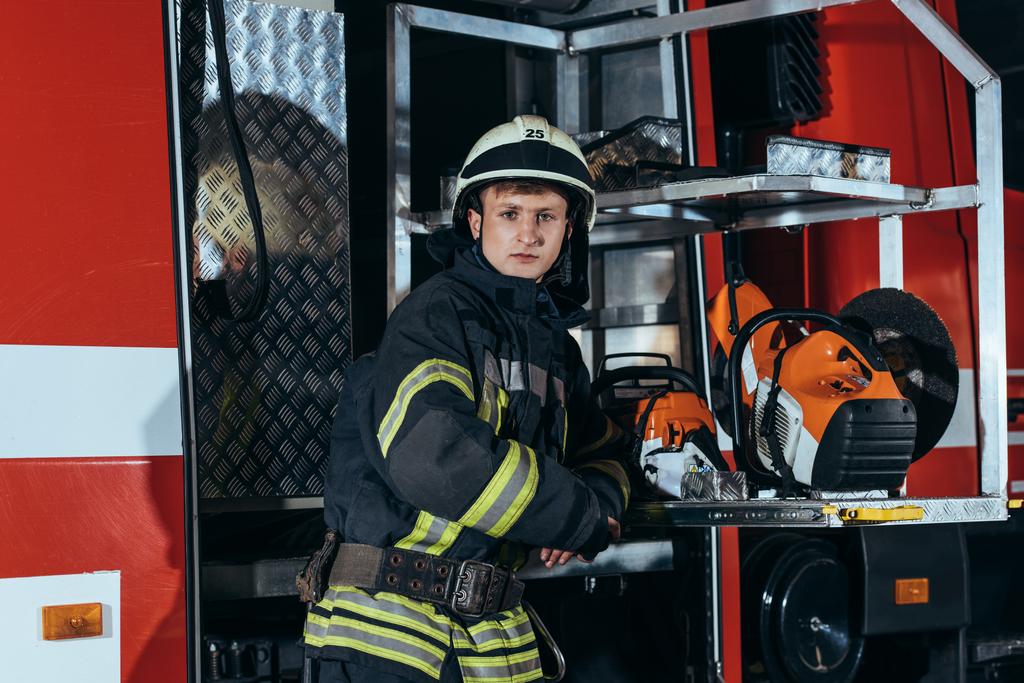 portrait of firefighter in helmet standing at truck at fire station - Photo, Image