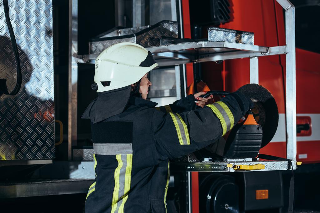 oldalnézetből női tűzoltó állandó a tűzoltóállomás teherautó felszerelés - Fotó, kép