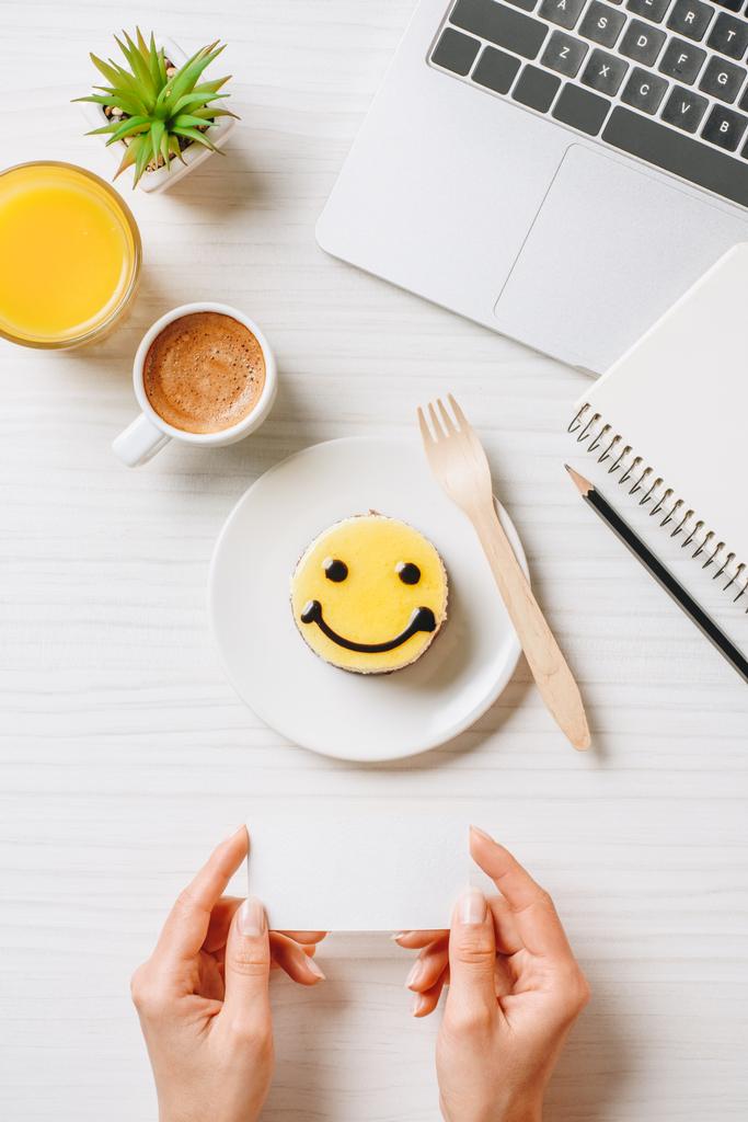 обрізане зображення бізнес-леді, що тримає порожню візитну картку за столом з апельсиновим соком, чашкою кави та тортами з символом посмішки в офісі
  - Фото, зображення