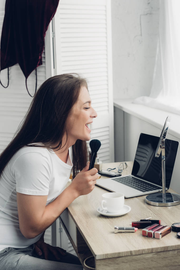 onnellinen transsukupuolinen nainen tekee meikkiä työpaikalla kotona - Valokuva, kuva
