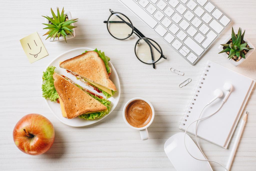 bovenaanzicht van werkplek met broodje, koffiekopje, apple en symbool van glimlach aan tafel in kantoor  - Foto, afbeelding
