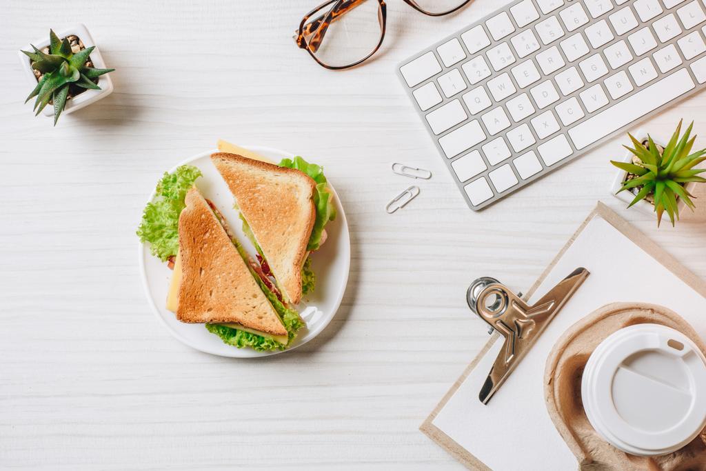 вид сверху одноразовой чашки кофе, сэндвич, компьютерная клавиатура и очки за столом в офисе
  - Фото, изображение