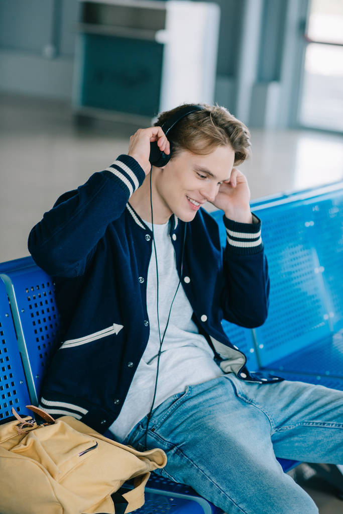 座っていると、空港でフライトを待っているヘッドフォンで若い男の笑みを浮かべてください。 - 写真・画像