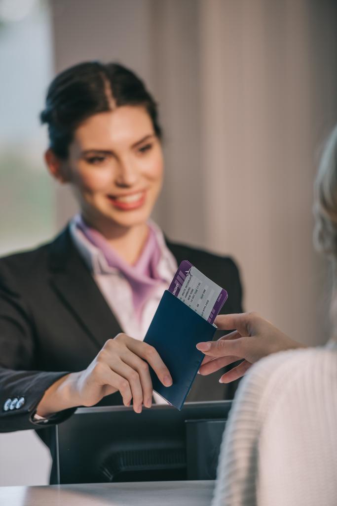 usmívající se letiště pracovník dává pas s palubní vstupenku na Mladý cestovatel na check-in přepážce  - Fotografie, Obrázek