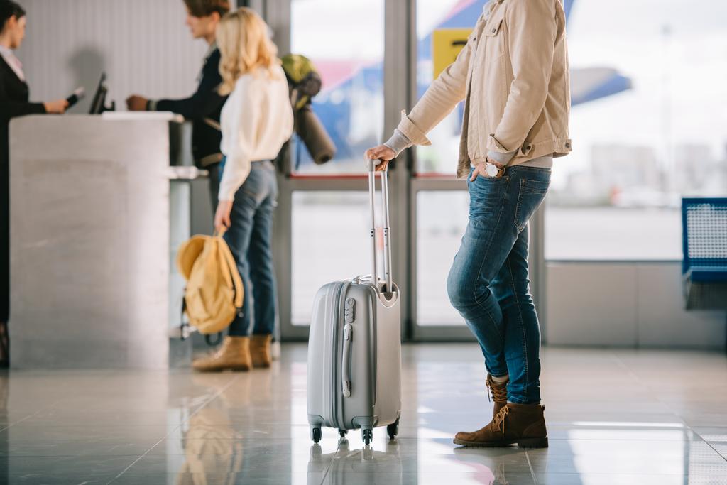 обрезанный снимок мужчины с чемоданом, стоящим возле стойки регистрации в аэропорту
 - Фото, изображение