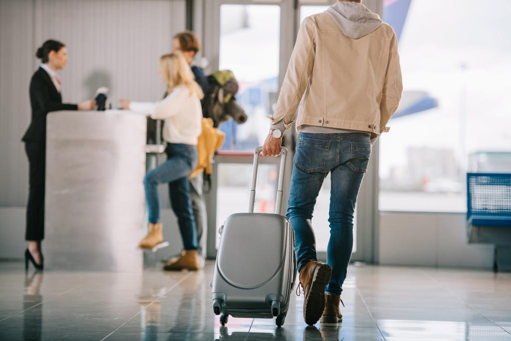 foto ritagliata di uomo con valigia che va al banco del check-in in aeroporto
 - Foto, immagini