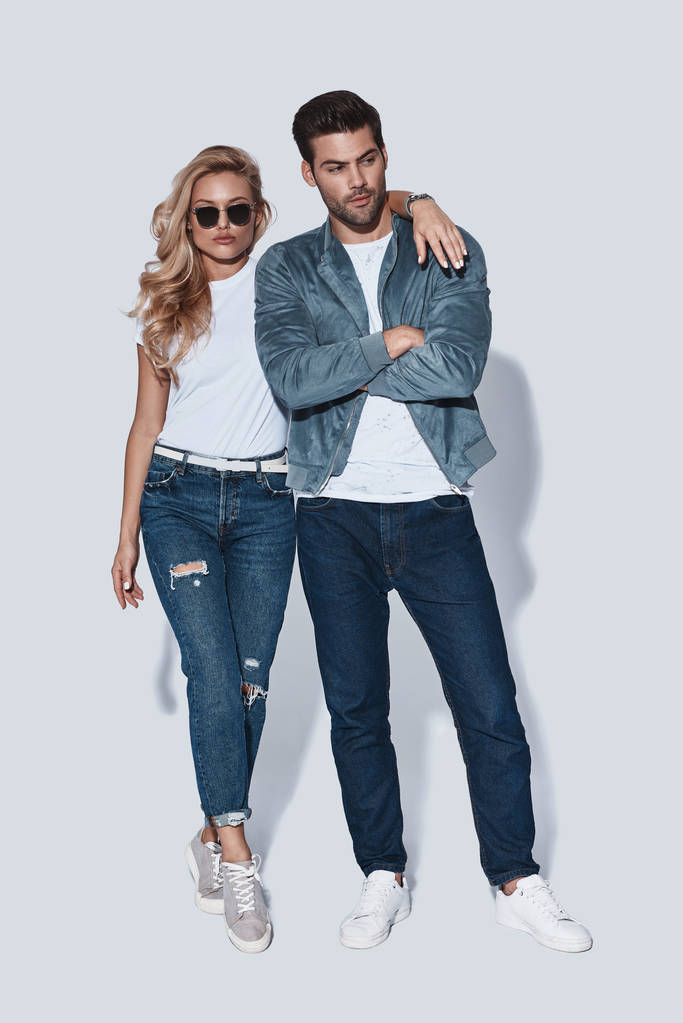 Krásná mladá dvojice v džínové oblečení, všeobjímající stoje šedé pozadí po celé délce - Fotografie, Obrázek