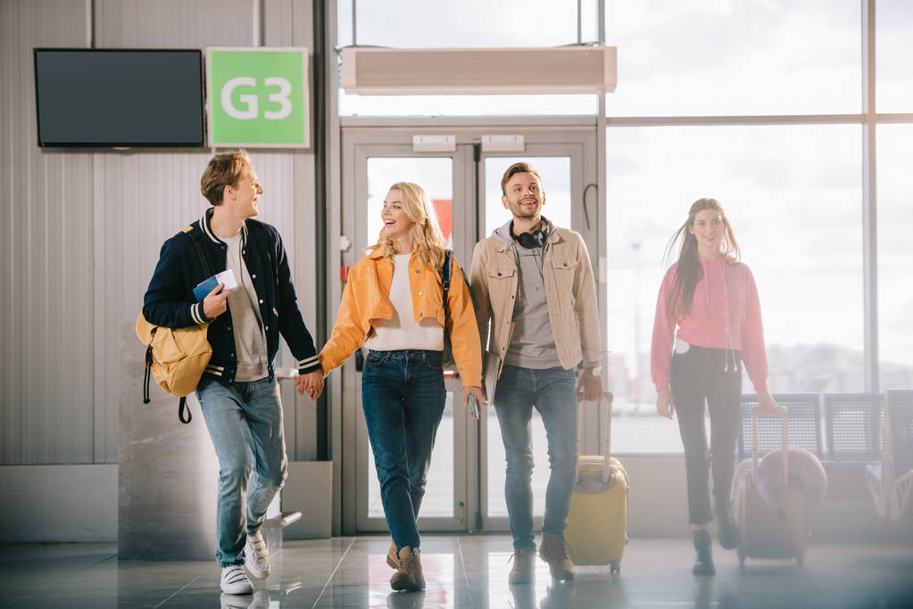 jóvenes felices con documentos y equipaje caminando en la terminal del aeropuerto
  - Foto, Imagen