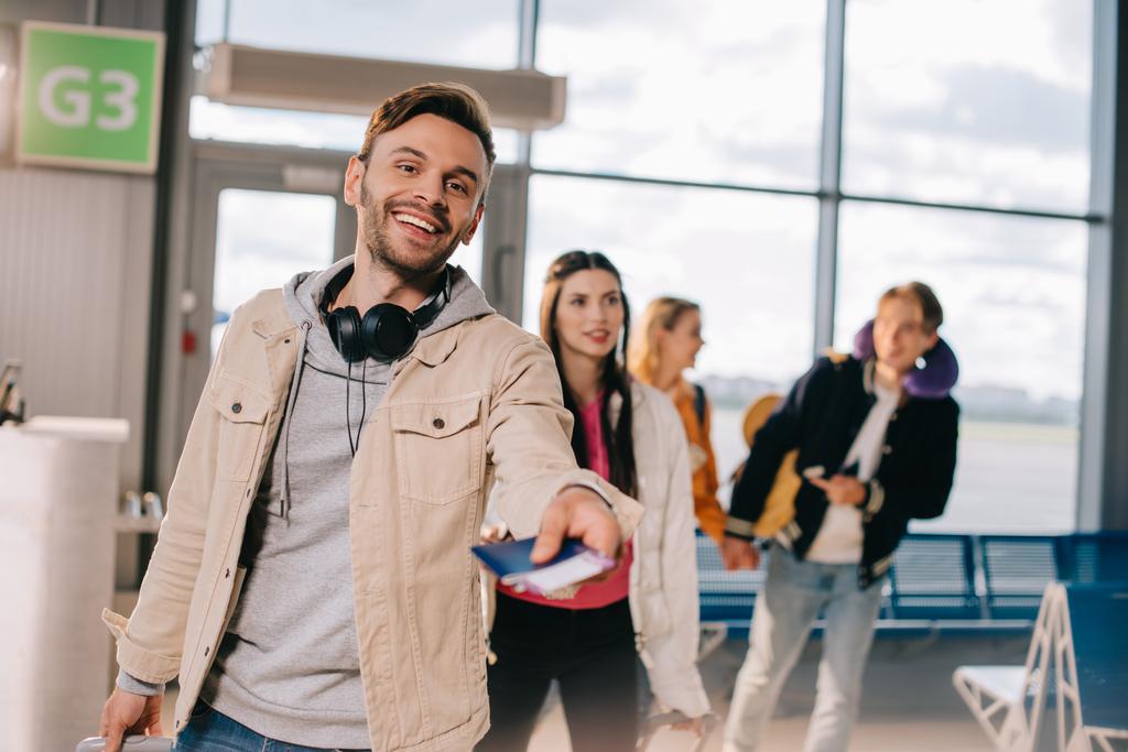 счастливый молодой человек с паспортом с посадочным талоном и улыбкой на камеру в аэропорту
 - Фото, изображение