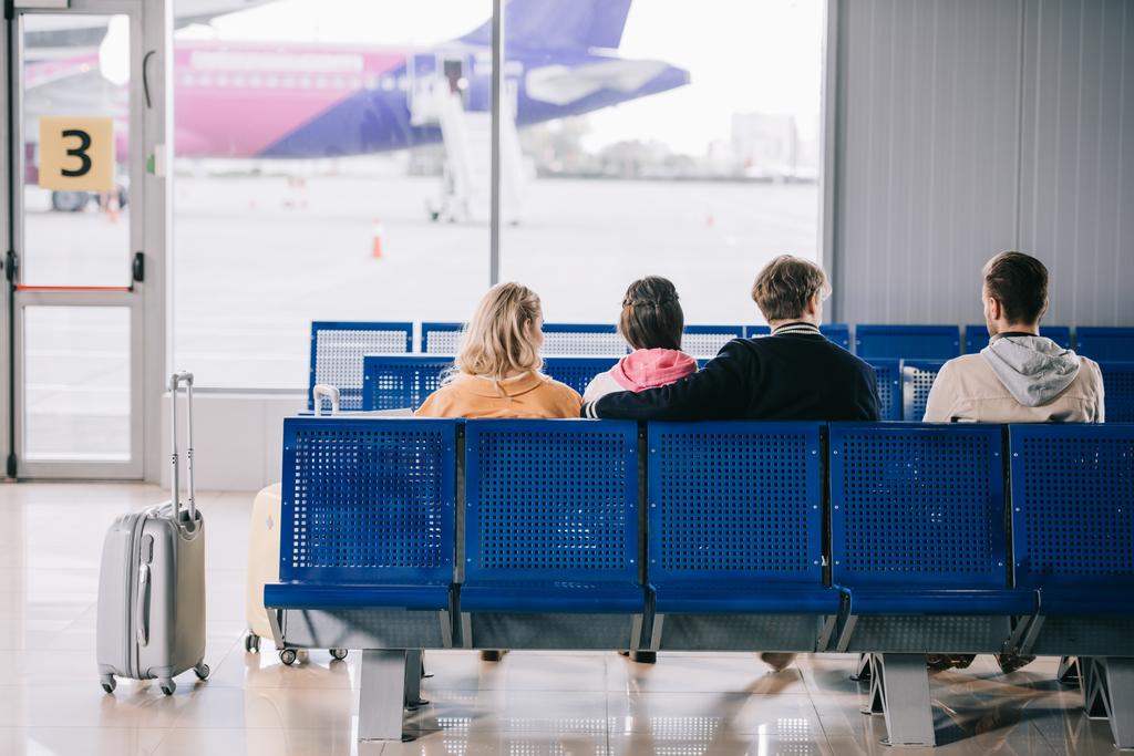 Rückansicht von jungen Menschen, die im Flughafenterminal sitzen und auf ihren Flug warten  - Foto, Bild