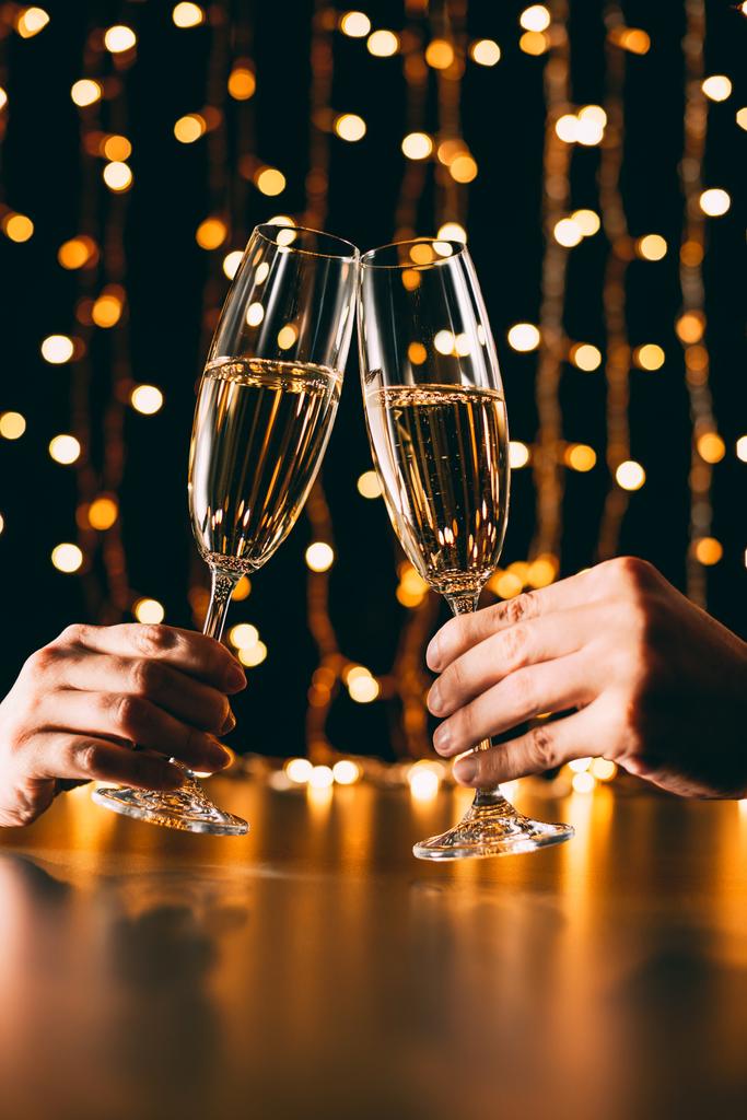 image recadrée de couple cliquetis avec des verres de champagne sur fond de guirlande, concept de Noël
 - Photo, image